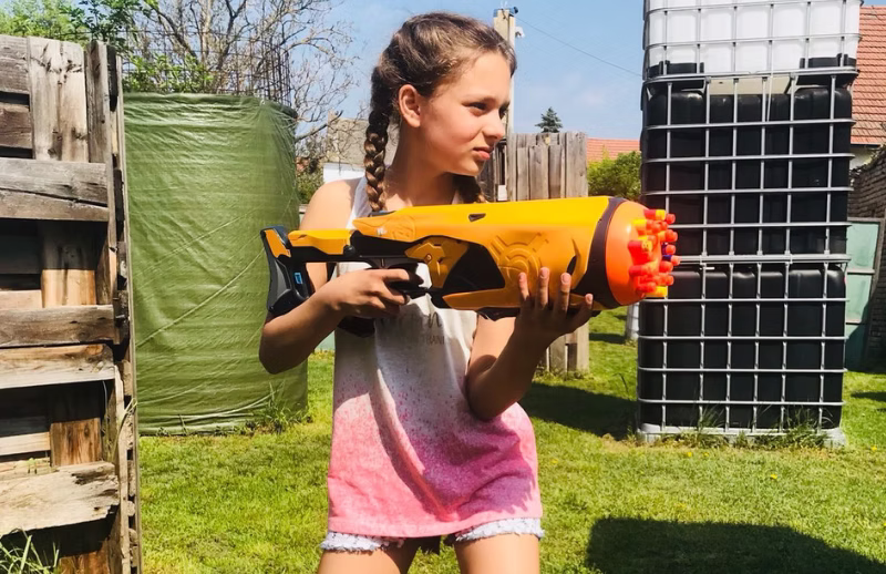 Nerftag-Spielerin mit gelbem Blaster an einer Deckung im Freien